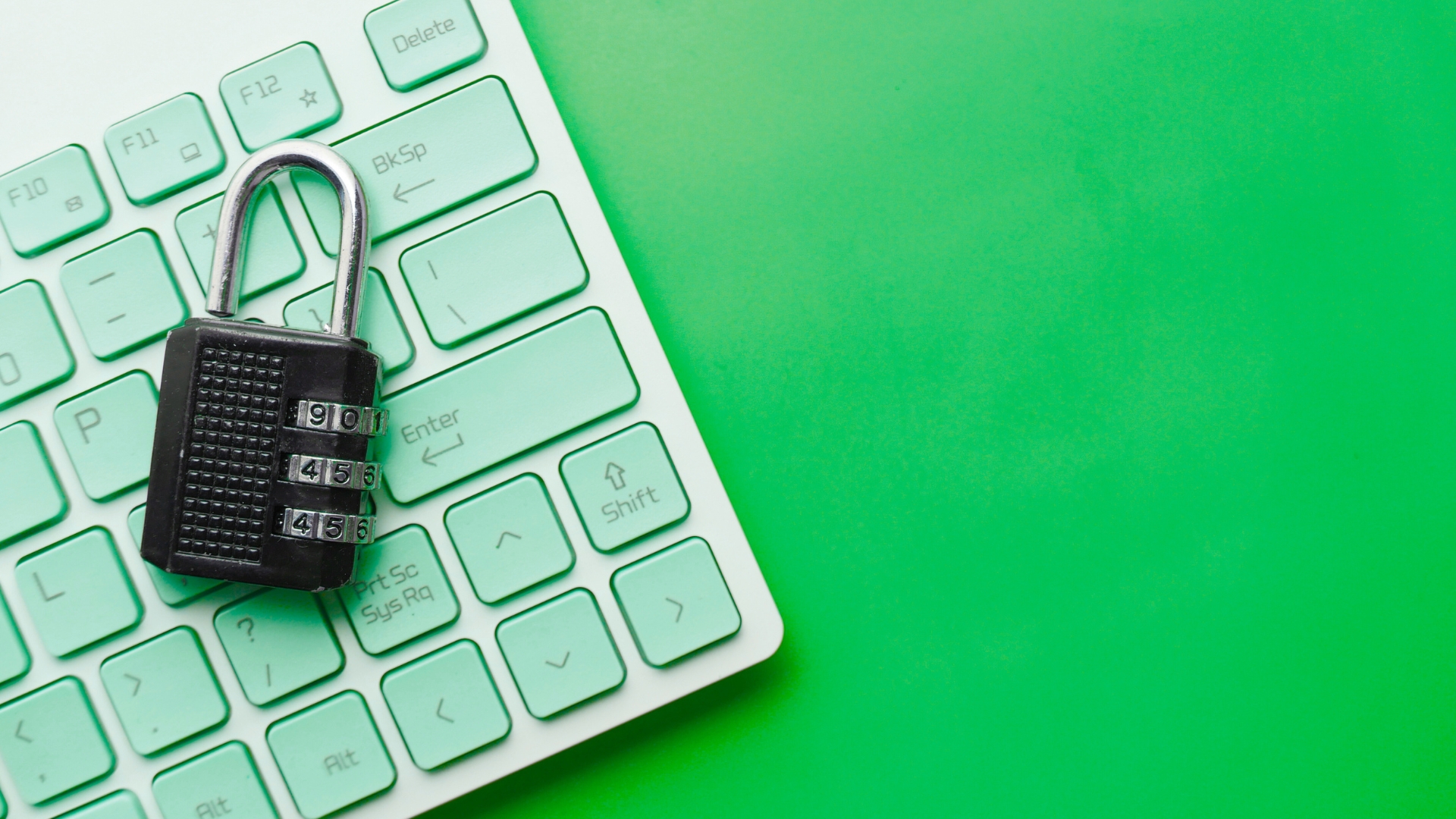 A black combination lock rests on a green keyboard against a matching green background, symbolizing cybersecurity.